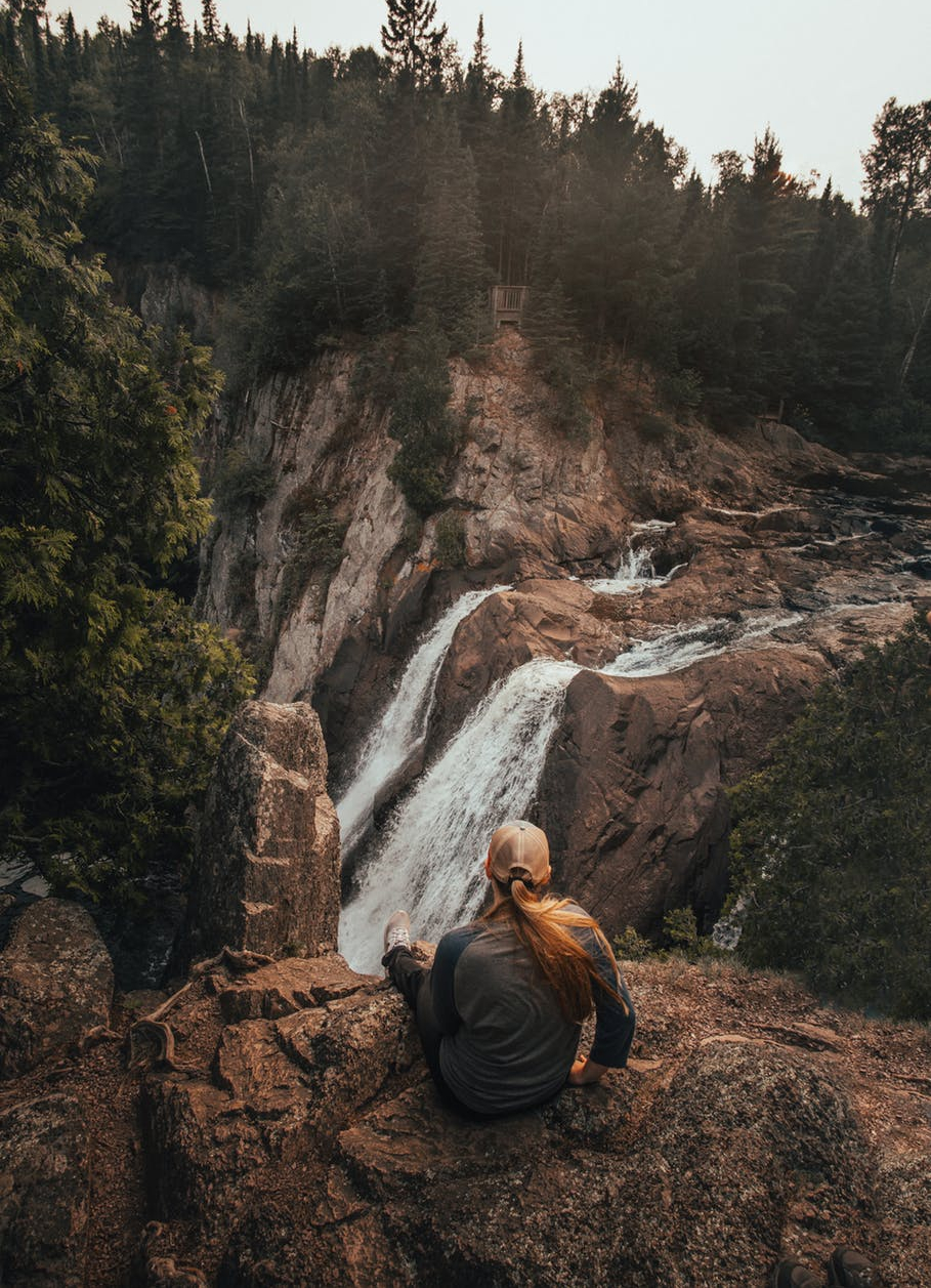 woman sitting on rock while staring on waterfall